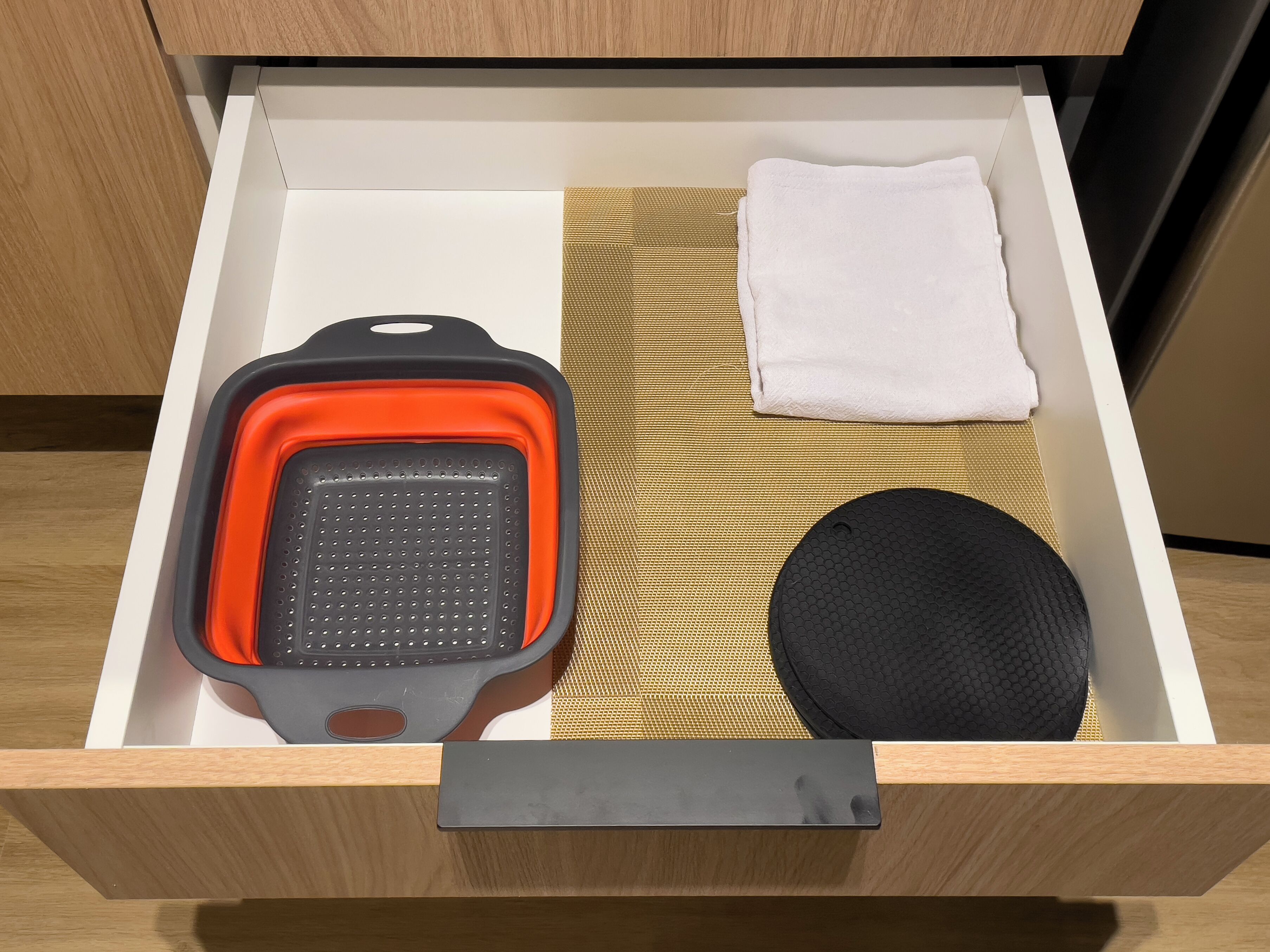 A drawer with a black and orange appliance, a white towel, and a black circular object.