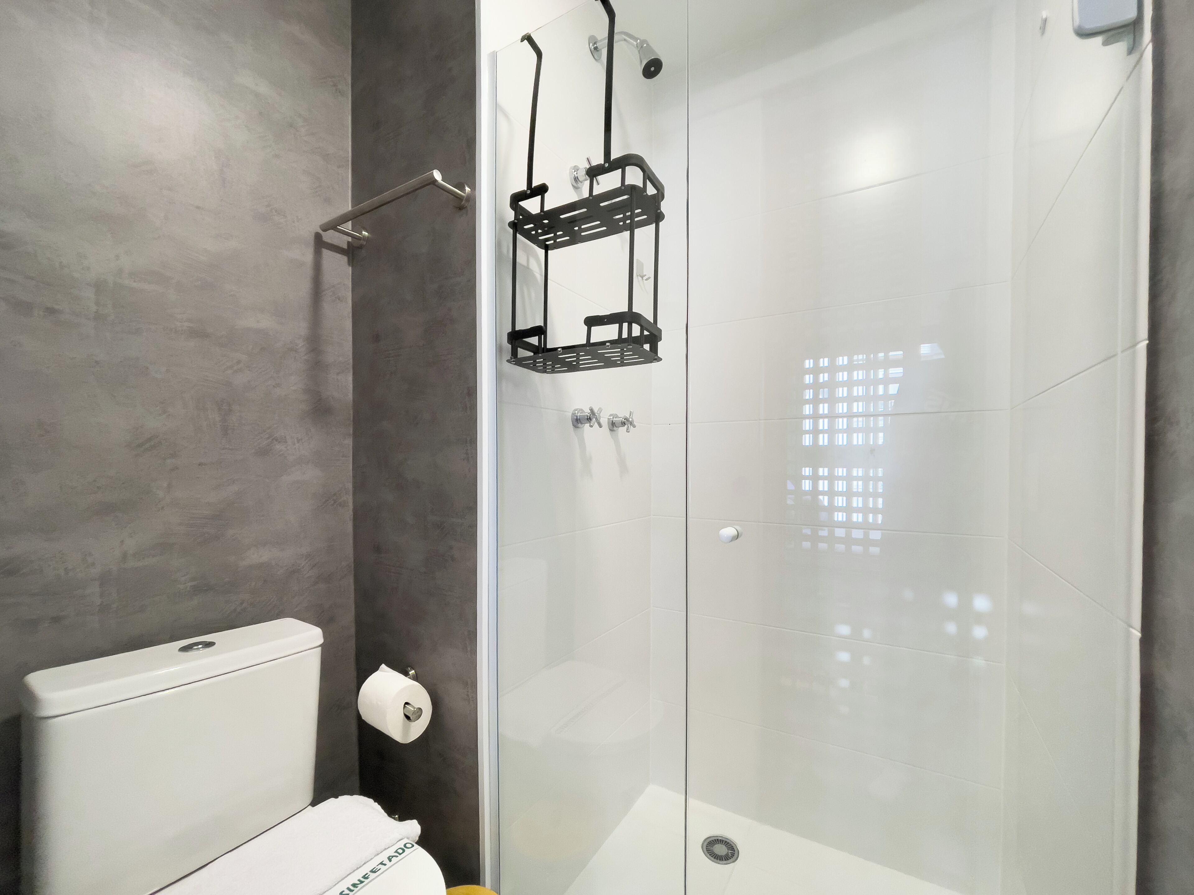 A modern bathroom with a glass shower enclosure, a toilet, and a towel rack.