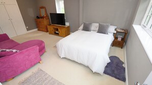 A bedroom with a bed, a TV, a dresser, and a pink sofa.