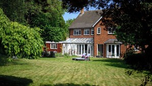 A two-story house with a well-maintained lawn, a conservatory, and a patio area with chairs.