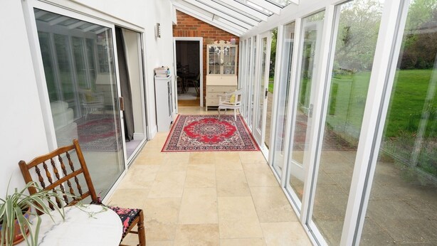 A sunlit corridor with a red patterned rug, leading to a room with a white cabinet and a dining area with a table and chairs.
