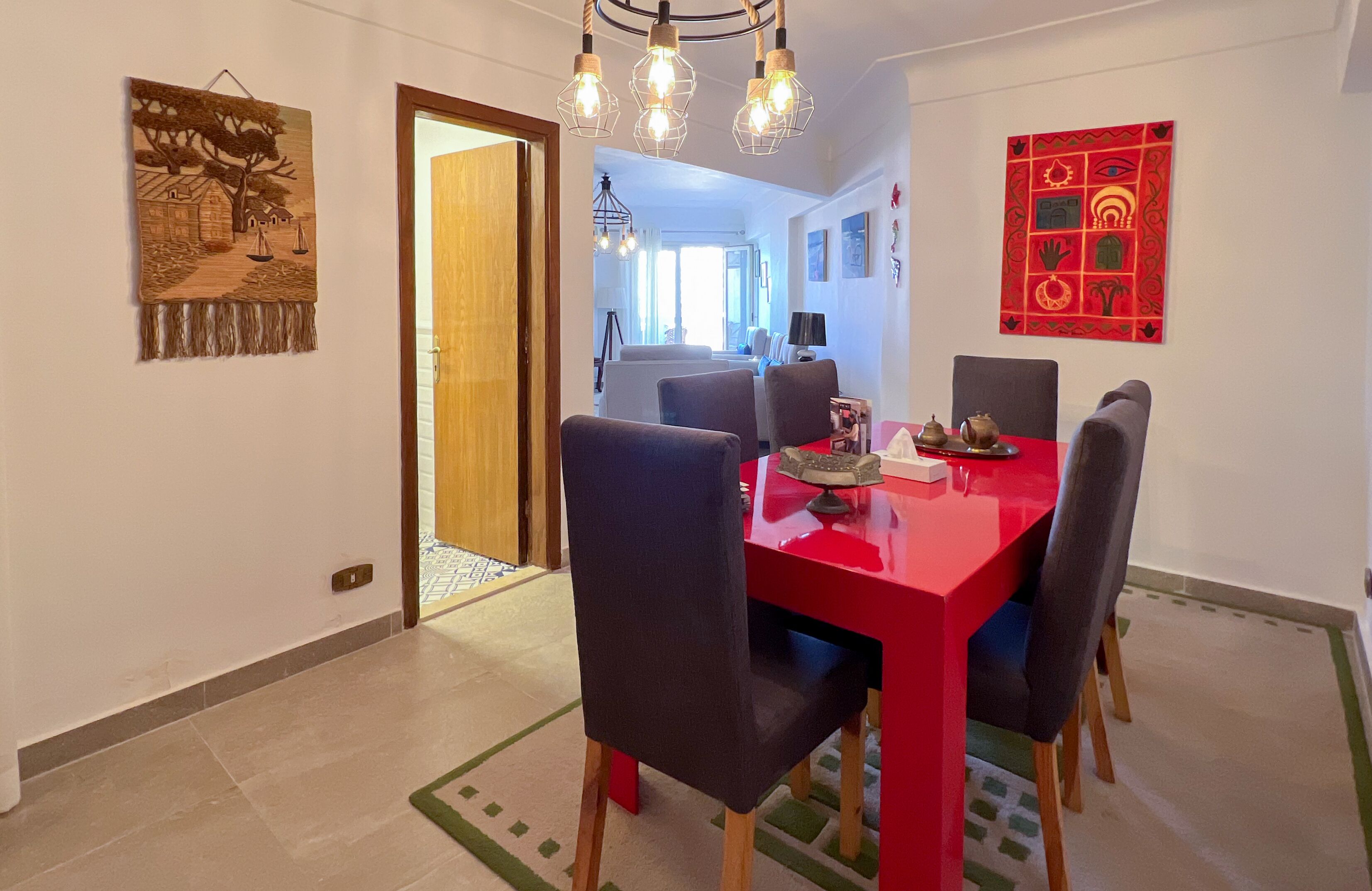 Un comedor con una mesa roja y sillas negras, una lámpara colgante y un adorno rojo en la pared.