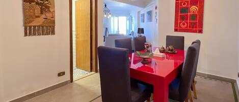 Un comedor con una mesa roja y sillas negras, una lámpara colgante y un adorno rojo en la pared.