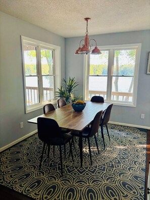 A dining area with a wooden table, chairs, a bowl of fruit, and a patterned rug.