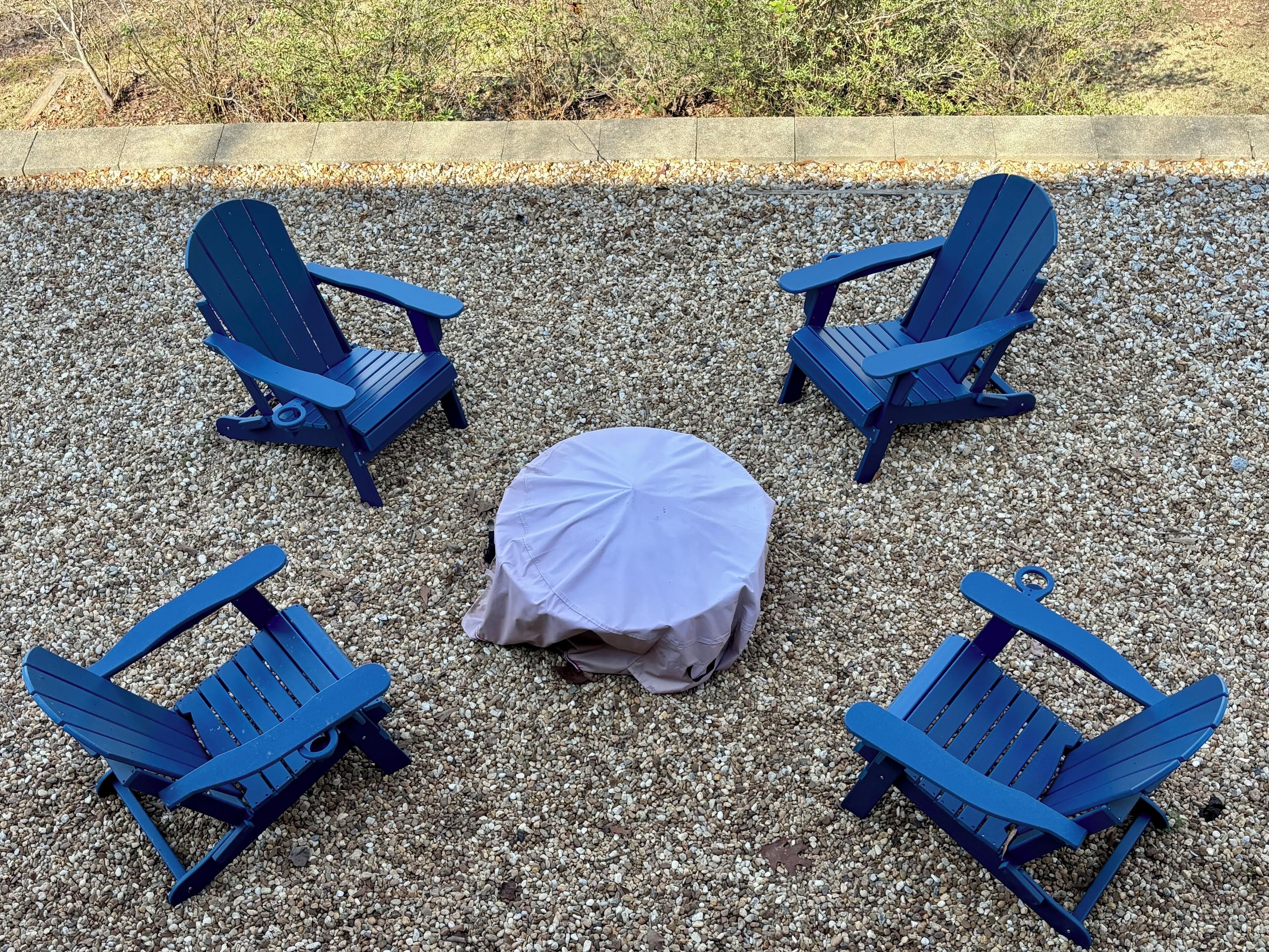 A seating arrangement with four blue Adirondack chairs and a round table covered with a white tablecloth.