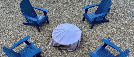 A seating arrangement with four blue Adirondack chairs and a round table covered with a white tablecloth.