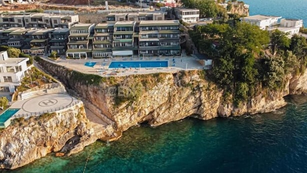 Et kysthotel med flere balkoner med udsigt over havet, et poolområde og en beliggenhed på en klippe.