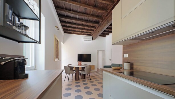 A modern kitchen with a wooden countertop, a coffee machine, and a dining area with hexagonal patterned flooring. - Cistern Elegant Comfort 2bdr (Roma)