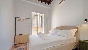 A hotel room with a bed, a wooden cabinet, a wall-mounted light, and a view through a window. - Cistern Elegant Comfort 2bdr (Roma)