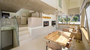 A modern kitchen with a dining area, a staircase, and a large window providing a view of the outdoors. - Seaside Luxury Immersed in Nature (Valbandon)