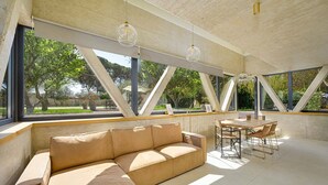 A modern interior with a beige sectional sofa, a dining table with chairs, and large windows offering a view of greenery outside. - Seaside Luxury Immersed in Nature (Valbandon)