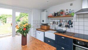 Une cuisine moderne avec des armoires blanches, un plan de travail en bois et un four encastré. Une fenêtre offre une vue sur un jardin, et les ustensiles de cuisine sont accrochés au mur.