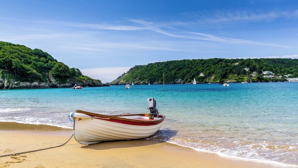 Un bateau sur une plage de sable, avec une eau turquoise cristalline et des collines verdoyantes en arrière-plan.