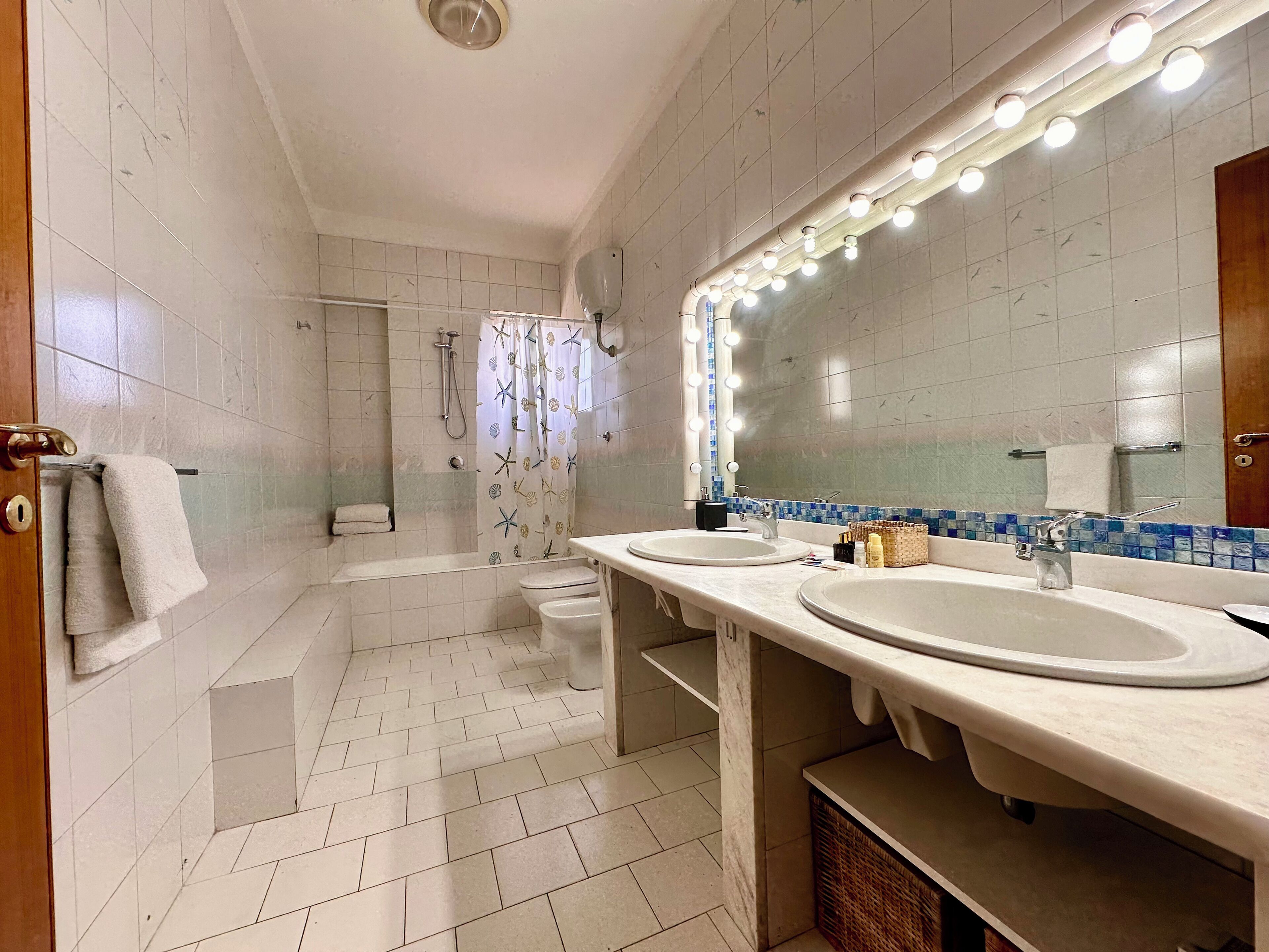 A bathroom with two sinks, a shower, and a vanity mirror with lights.