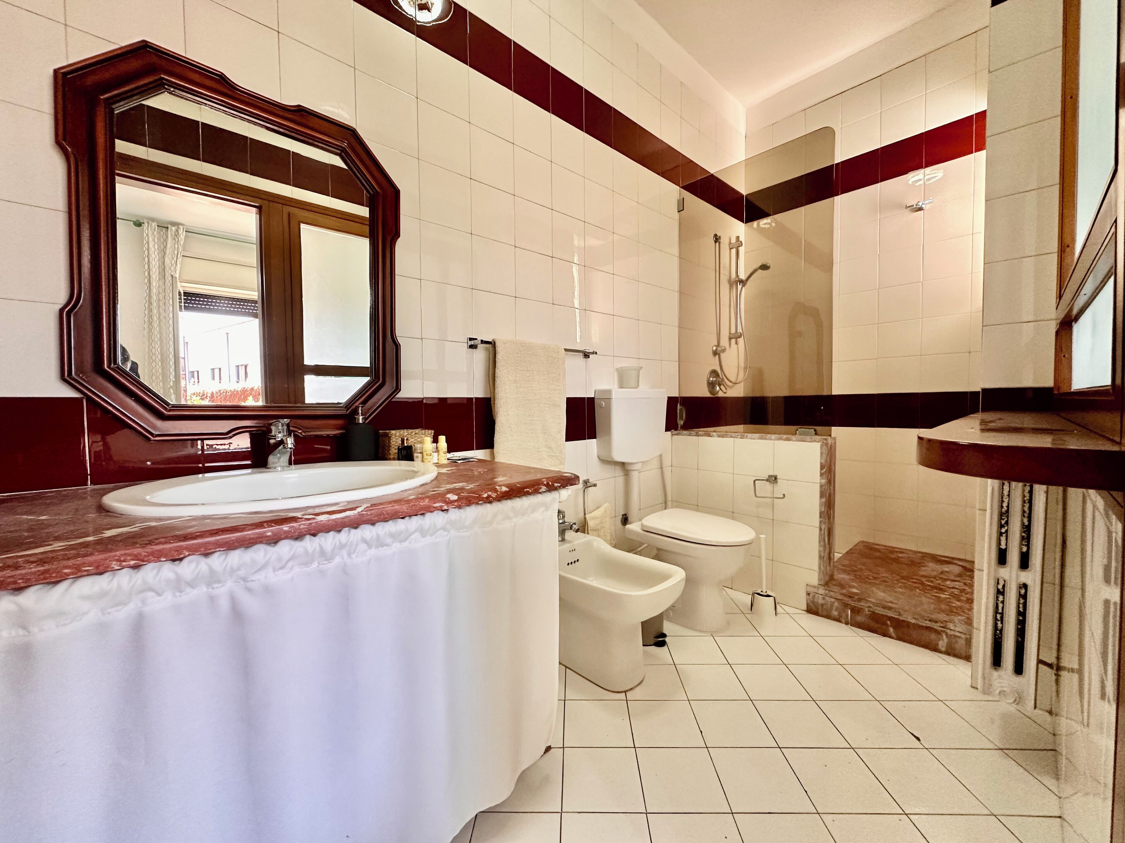 A modern bathroom with a marble sink, a large mirror, a toilet, and a shower area.