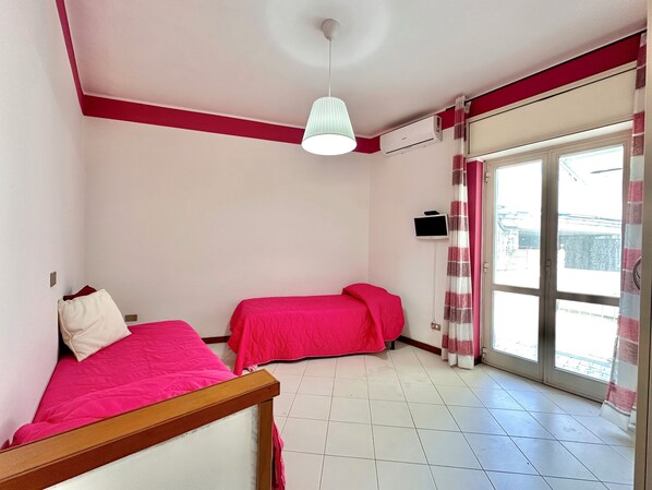 A bedroom with two beds, a ceiling light, an air conditioning unit, a TV, and a sliding glass door to the outside. - B&B Holiday (Torre Annunziata)