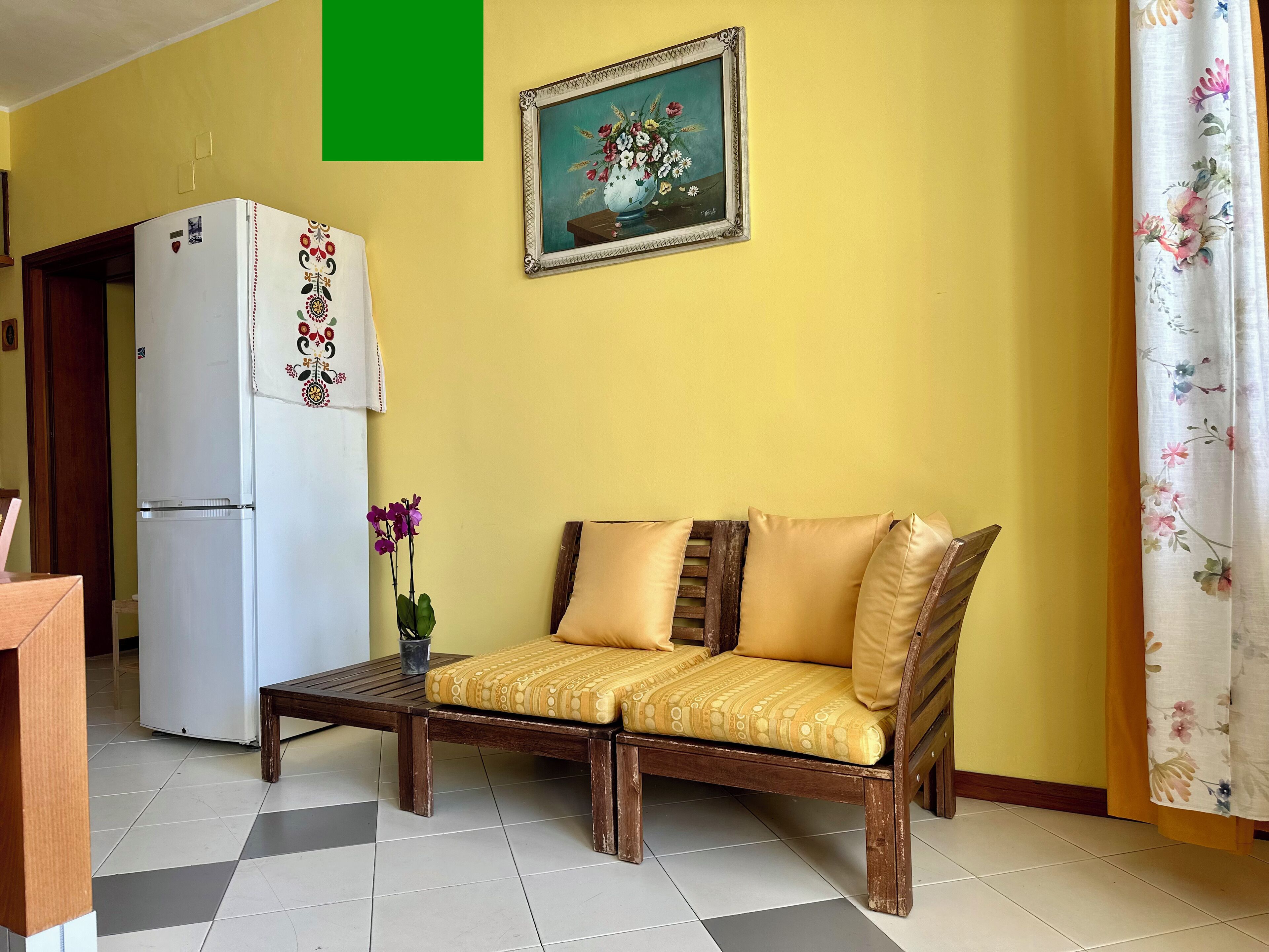 A living room with a sofa, a table, a refrigerator, and a painting on the wall.