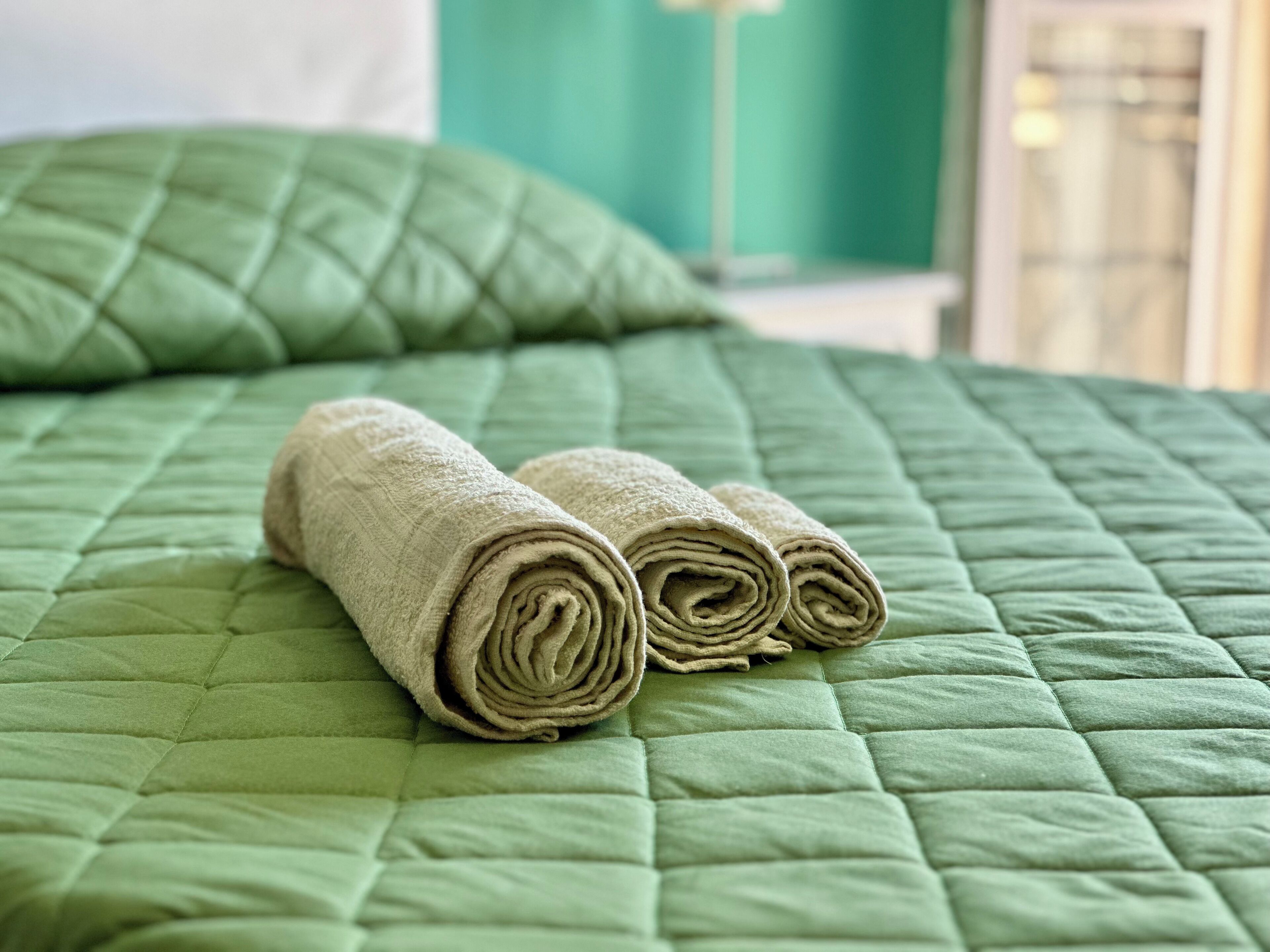 Una cama bien hecha con un edredón verde y dos toallas enrolladas.