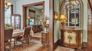 Un coin repas avec une table et des chaises en bois, un miroir doté d’un cadre orné et une lampe posée sur une petite table d’appoint.