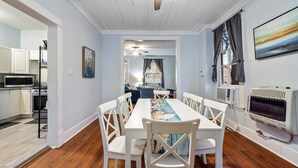 Un espace repas avec une longue table, des chaises blanches et un ventilateur de plafond.