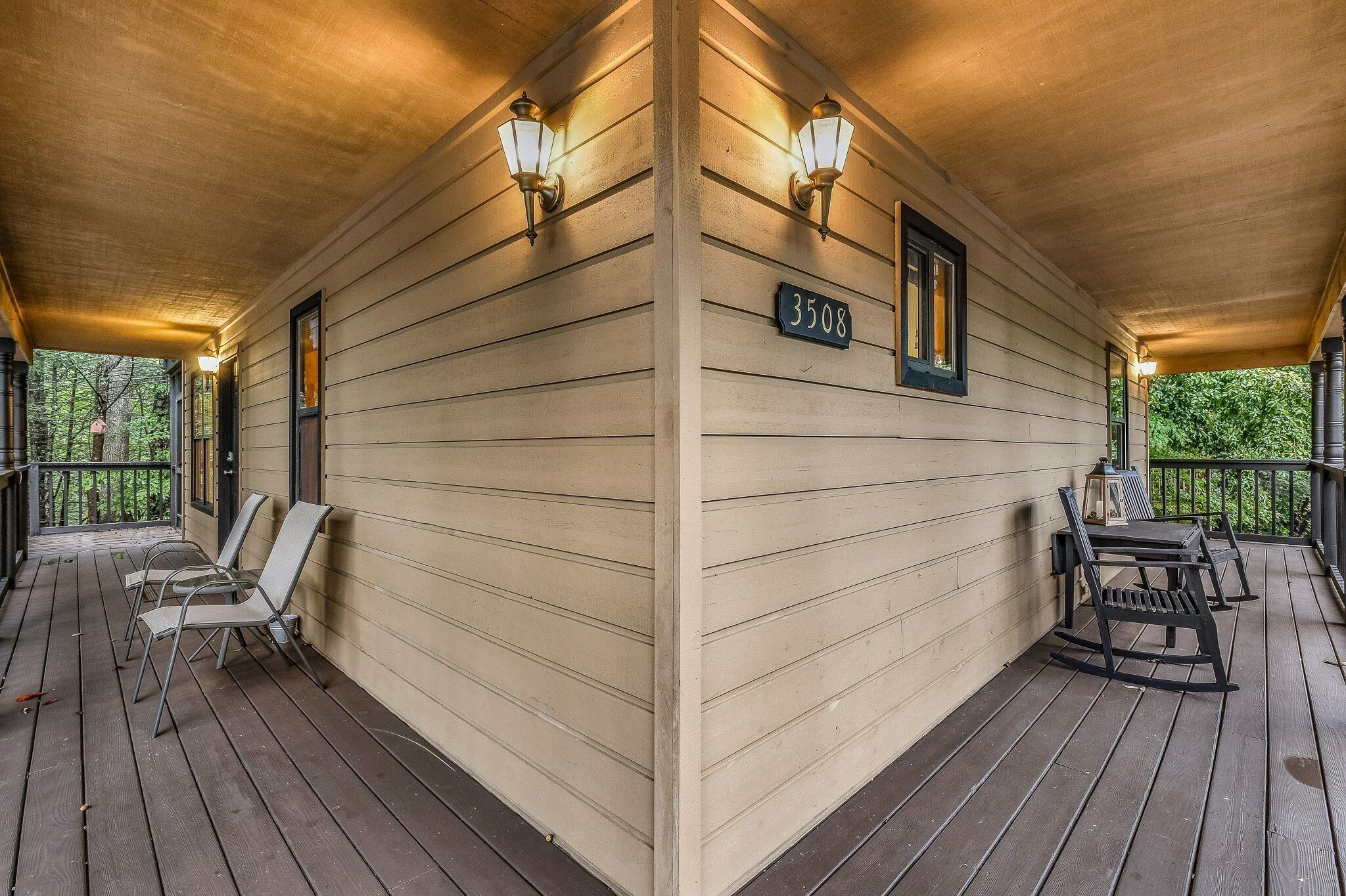 Un porche de madera con letrero de número, mobiliario exterior e iluminación en la pared.