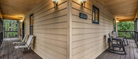 Un porche de madera con letrero de número, mobiliario exterior e iluminación en la pared.