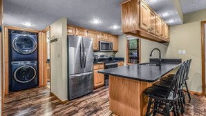 A modern kitchen with wooden cabinets, stainless steel appliances, and a central island with bar stools. - Count Your Blessings 3 Bedroom Home (Pigeon Forge)