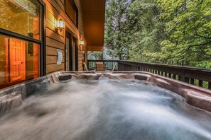 A hot tub on a wooden deck with a view of a forest. - Count Your Blessings 3 Bedroom Home (Pigeon Forge)