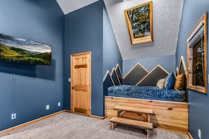 A room with a blue wall, a wooden door, a blue sofa with cushions, and a mounted TV displaying a landscape. - Count Your Blessings 3 Bedroom Home (Pigeon Forge)