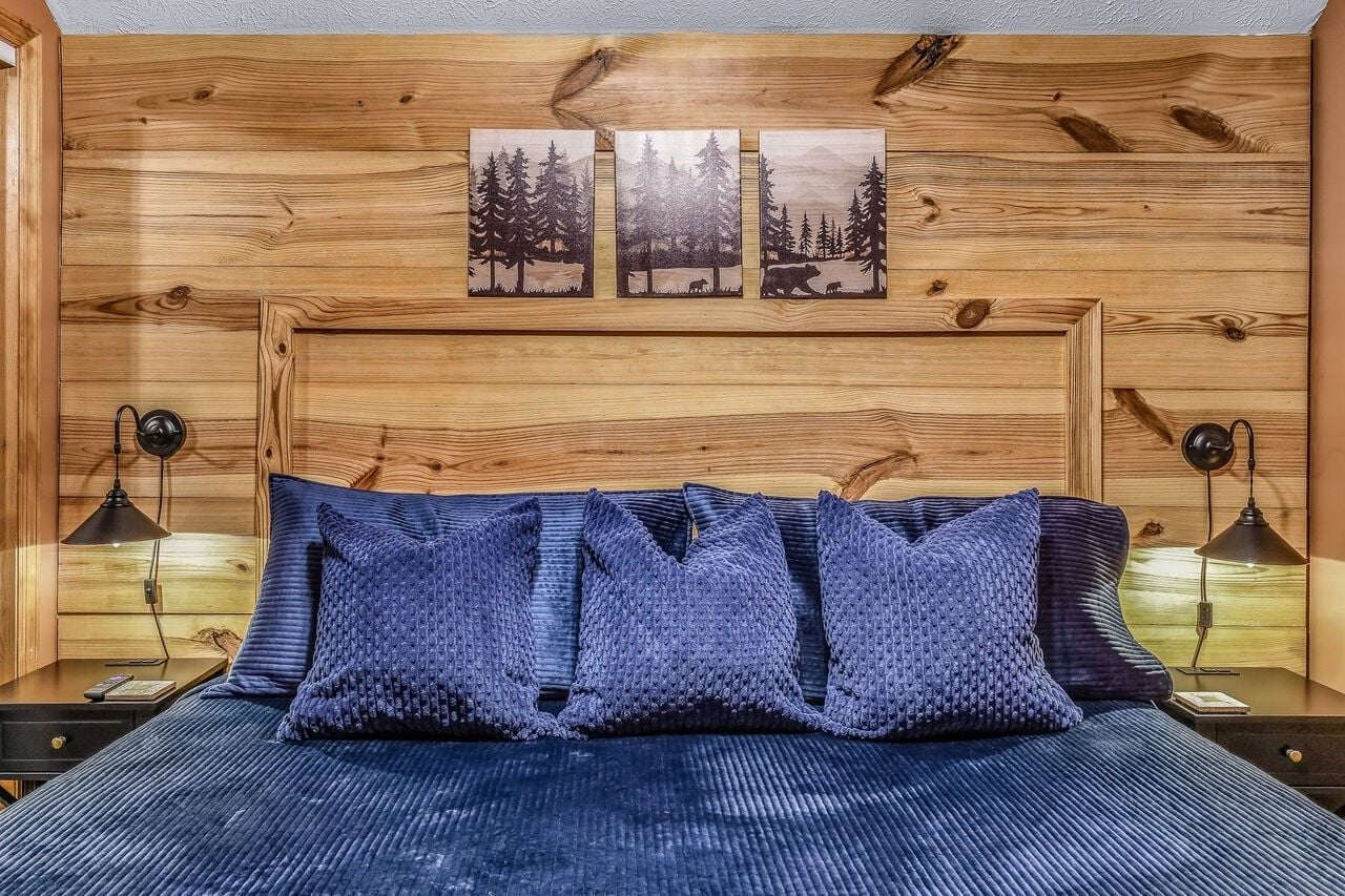 A bedroom with a wooden headboard, a bed with blue bedding, and three wall-mounted picture frames depicting forest scenes.