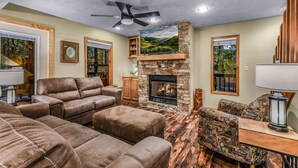 A cozy living room with leather sofas, a stone fireplace, and a ceiling fan. - Count Your Blessings 3 Bedroom Home (Pigeon Forge)