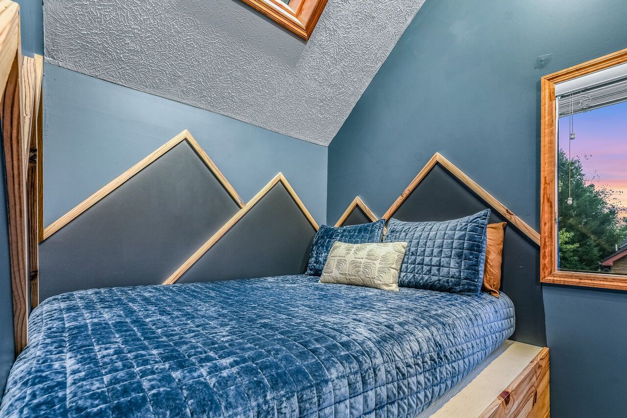 A bedroom with a bed, a sloped ceiling, and a window with a view.
