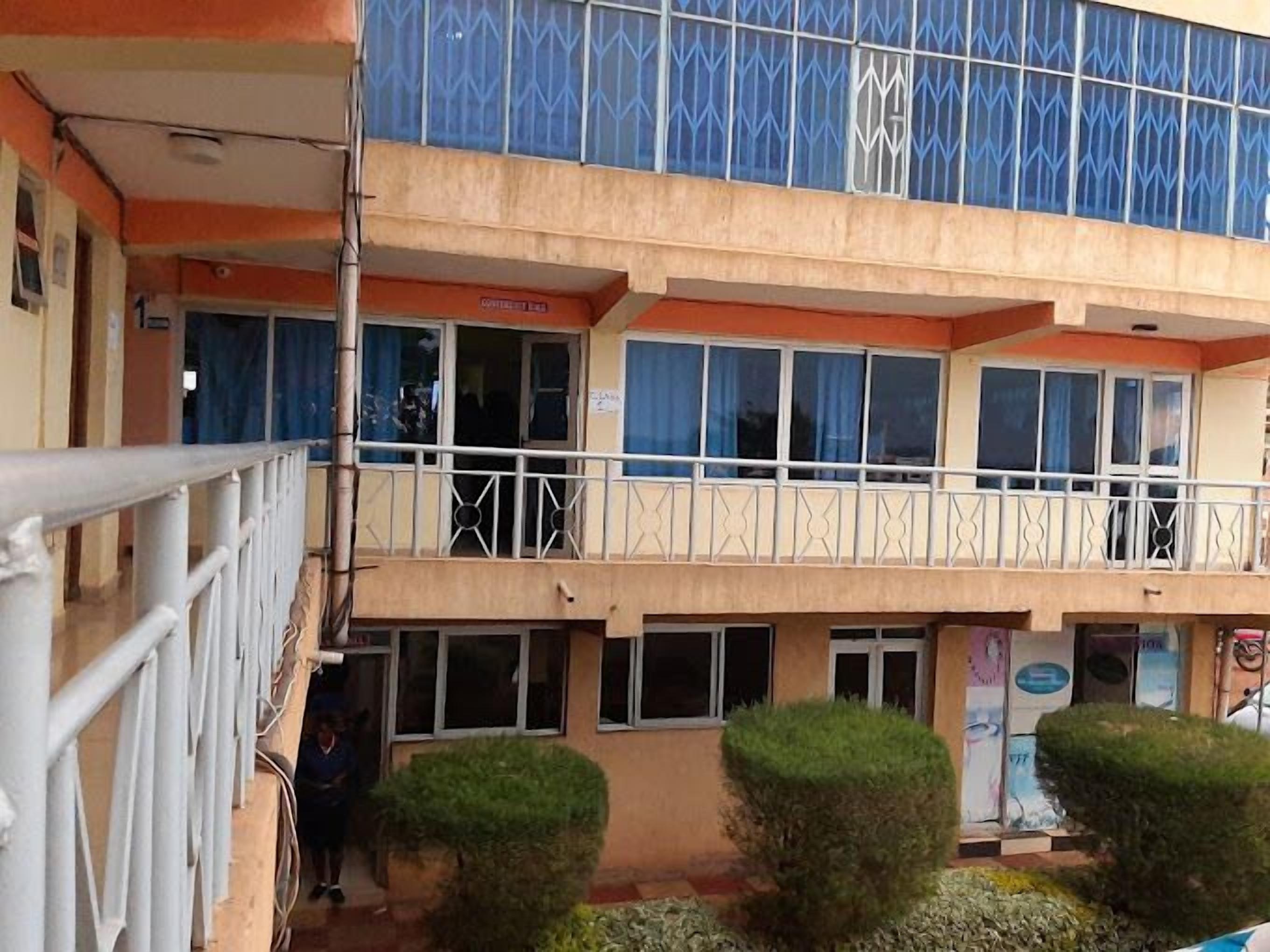 A multi-story building with balconies, a gated entrance, and a small garden area.