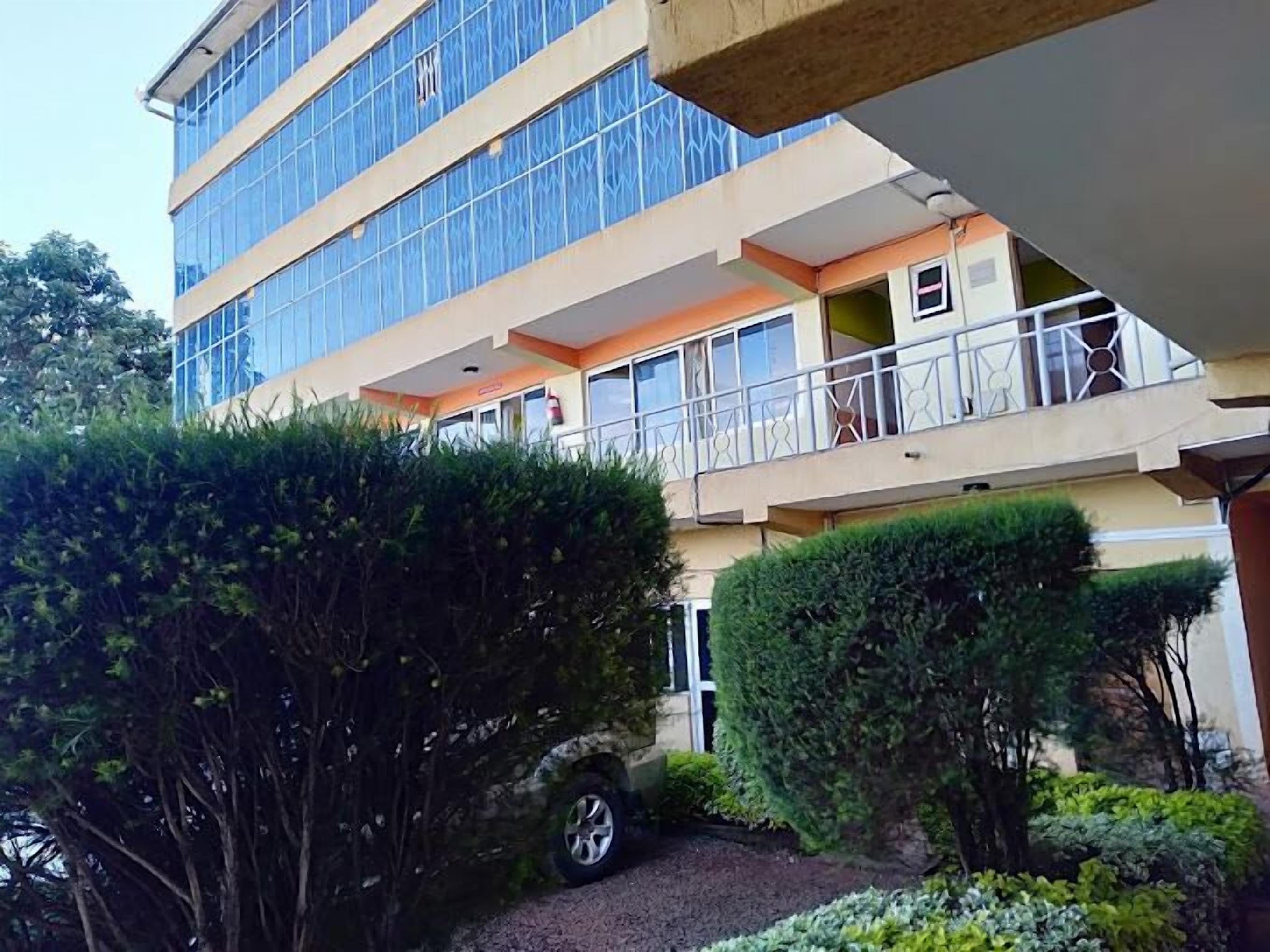 A multi-story building with balconies, a gravel driveway, and well-maintained greenery.