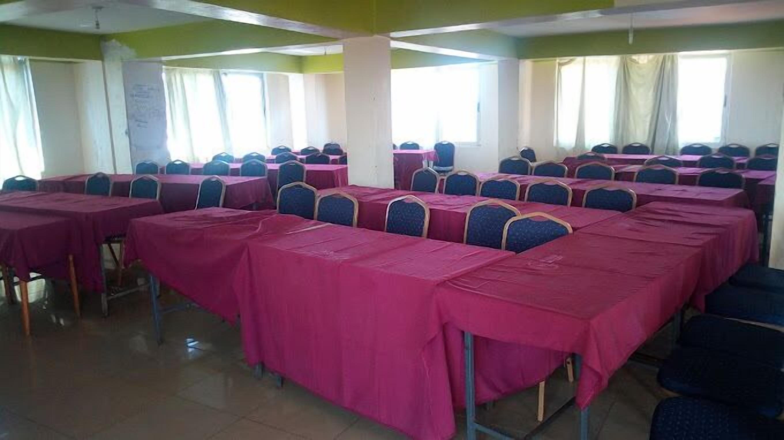 A conference room with rows of tables and chairs, large windows, and a tiled floor.