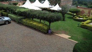 A well-maintained garden with neatly trimmed hedges, a gravel path, and a parked car. - The Guardian Hotel Nyamira (Nyamira)