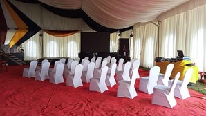 A conference room with rows of white chairs, a stage with a podium, and a red carpet. - The Guardian Hotel Nyamira (Nyamira)