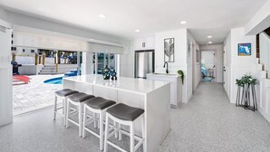 A modern kitchen with a central island, bar stools, and a view of a swimming pool. - 🌊Bay Front with Private Pool and Tiki Bar-Bayview Beach House🌊 (Fort Myers Beach)