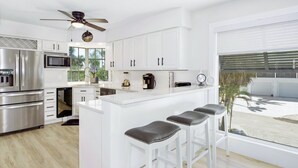 A modern kitchen with white cabinetry, stainless steel appliances, and a bar area with stools. - 🌊Bay Front with Private Pool and Tiki Bar-Bayview Beach House🌊 (Fort Myers Beach)