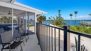 A covered outdoor seating area with chairs and tables, overlooking a beach with palm trees and a pier. - 🌊Bay Front with Private Pool and Tiki Bar-Bayview Beach House🌊 (Fort Myers Beach)