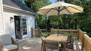 A wooden deck with a table and chairs, a wicker chair, and a large umbrella. - Charming 4-bedroom House on beautiful farm in Clear Brook with lovely views (Clear Brook)
