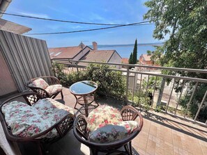 Un balcone con sedie in vimini e un tavolo in vetro, con vista su una zona residenziale con case e un corpo d'acqua.