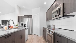 Uma cozinha moderna com eletrodomésticos de aço inoxidável, armários de madeira e painel de azulejos branco.