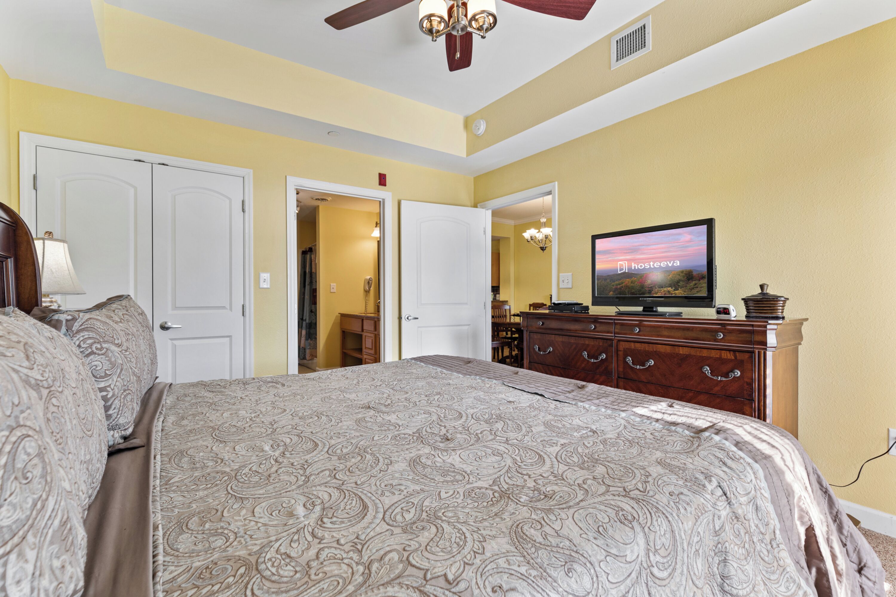 A bedroom with a large bed, a dresser, a television, and a ceiling fan.