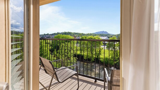 A balcony with a view of a river, greenery, and distant mountains.
