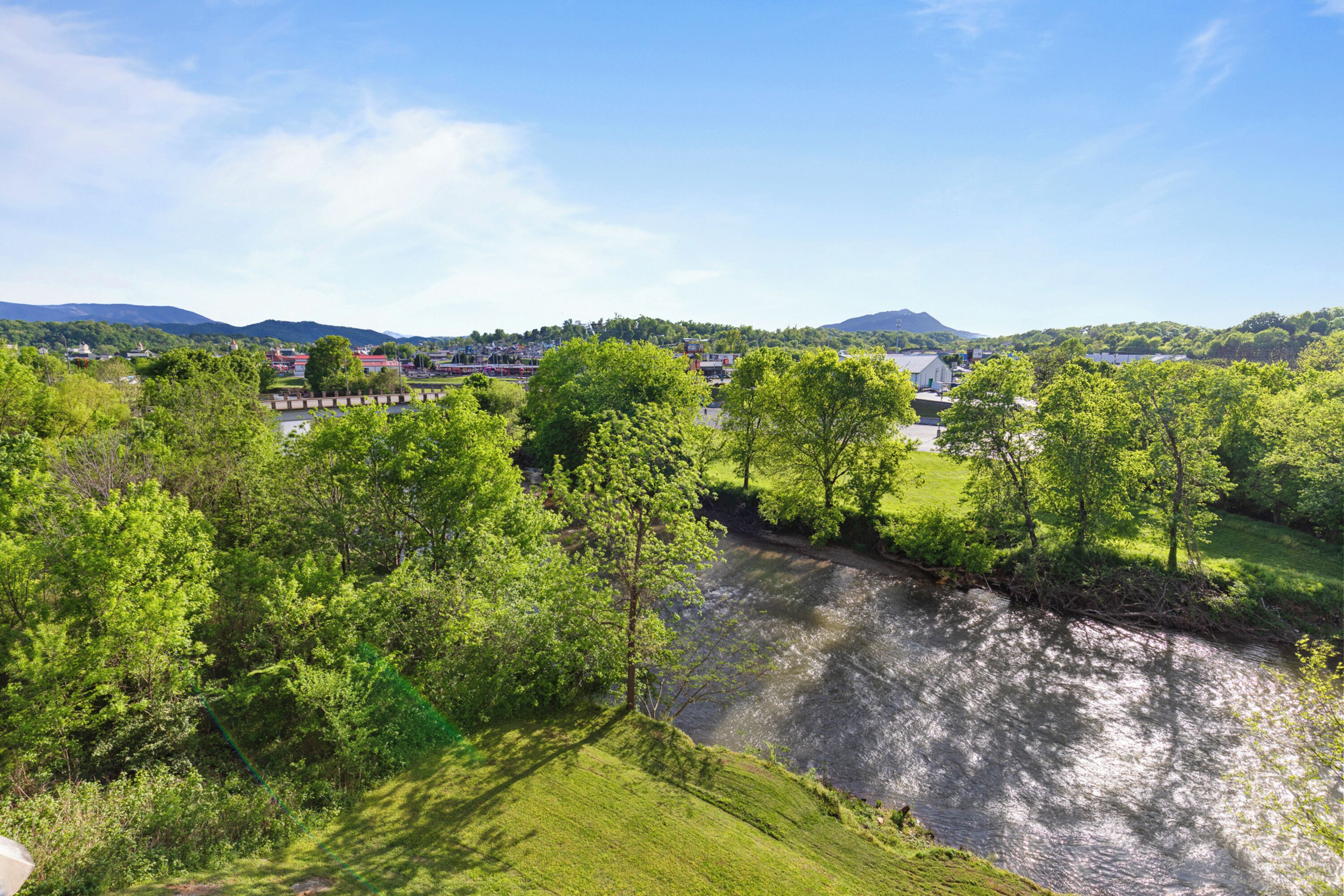 Ein Fluss fließt durch eine grüne Landschaft mit Bäumen und einer Stadt im Hintergrund.