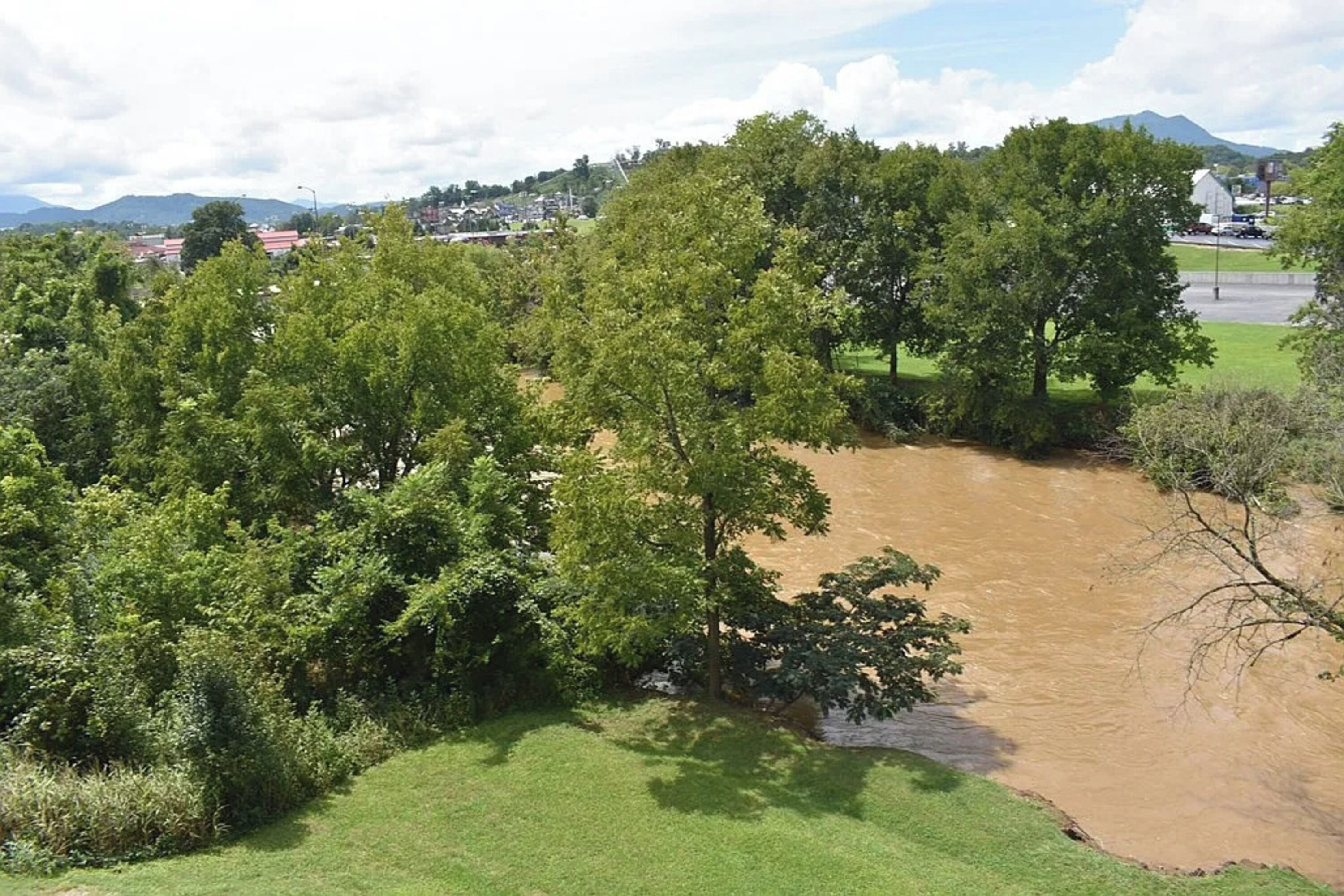 A river flowing through a green landscape with trees and a distant town.