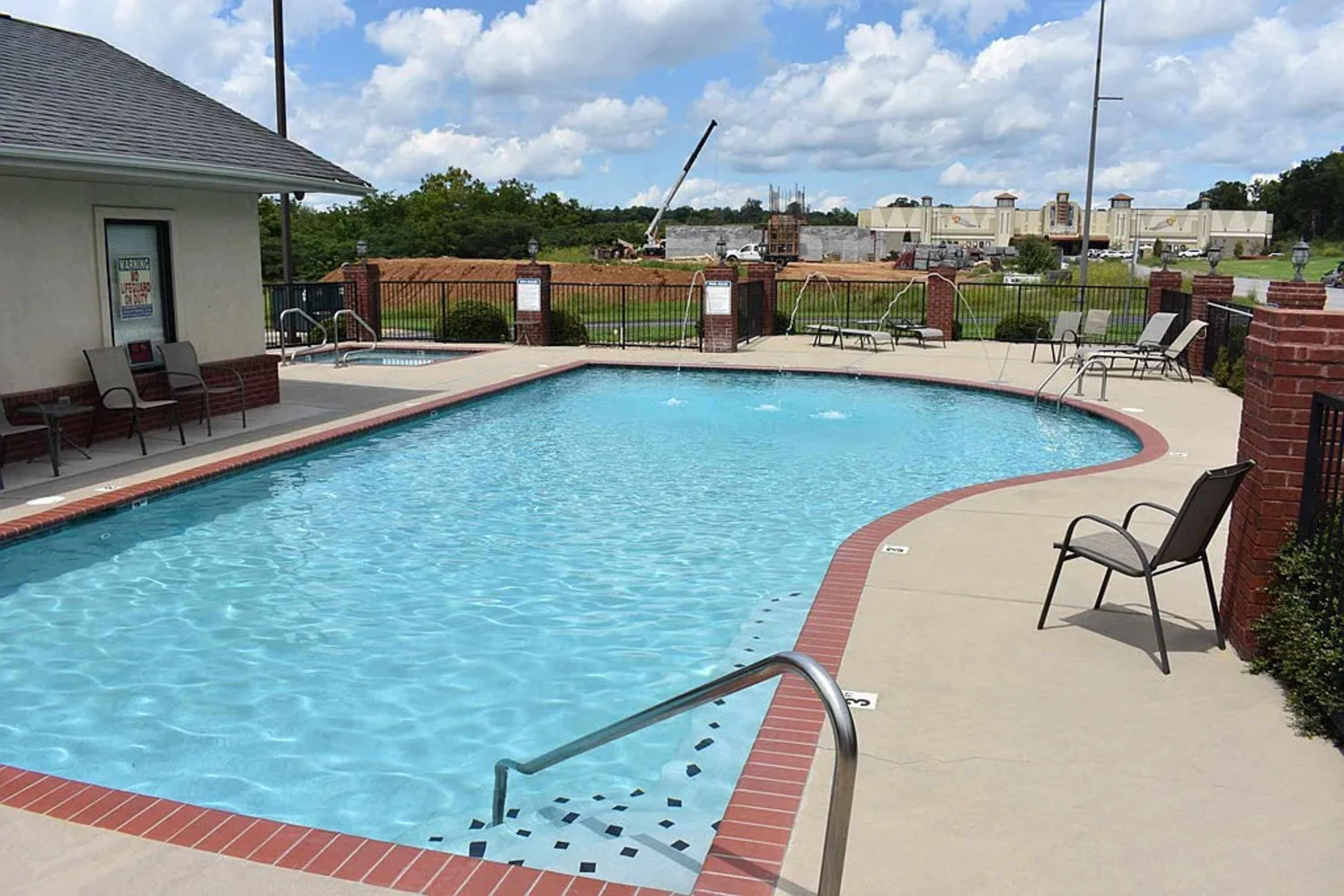 A rectangular swimming pool with a red border, surrounded by a brick walkway and lounge chairs.