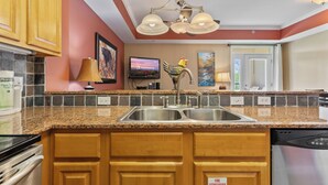 A kitchen with granite countertops, stainless steel appliances, wooden cabinets, a two-basin sink, and a ceiling light fixture.