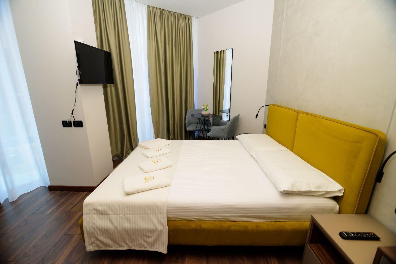 Una habitación de hotel con cama, televisión en la pared, escritorio con silla y ventana con cortinas.